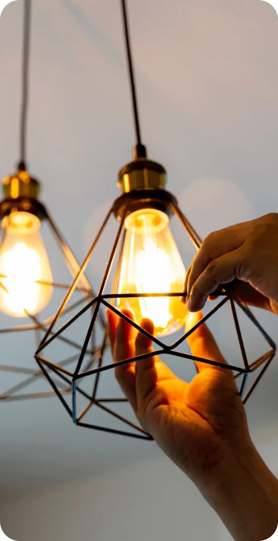 Hands adjusting decorative hanging light bulb.
