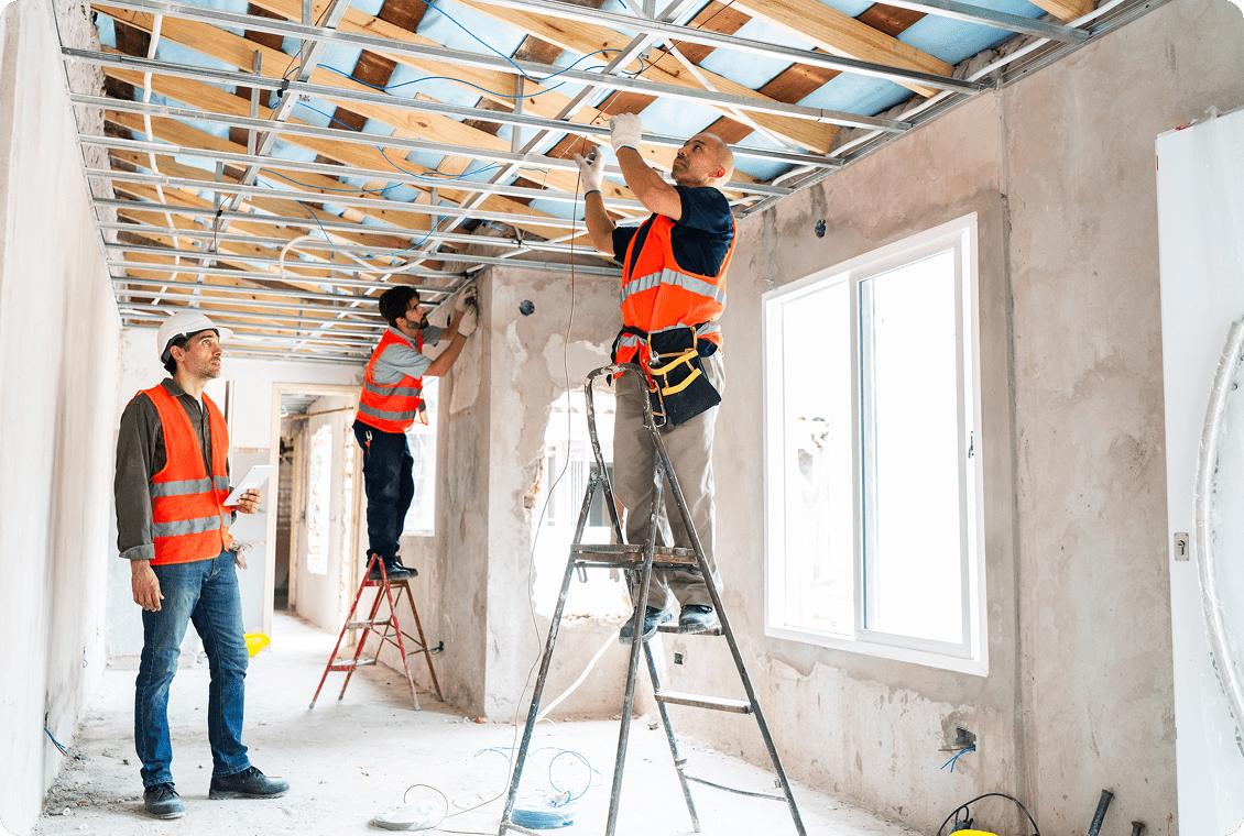 Construction workers installing ceiling framework indoors.