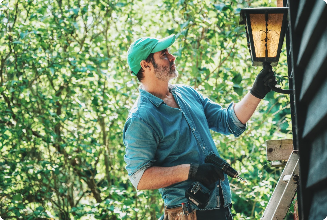 Man installing outdoor lantern on house wall.
