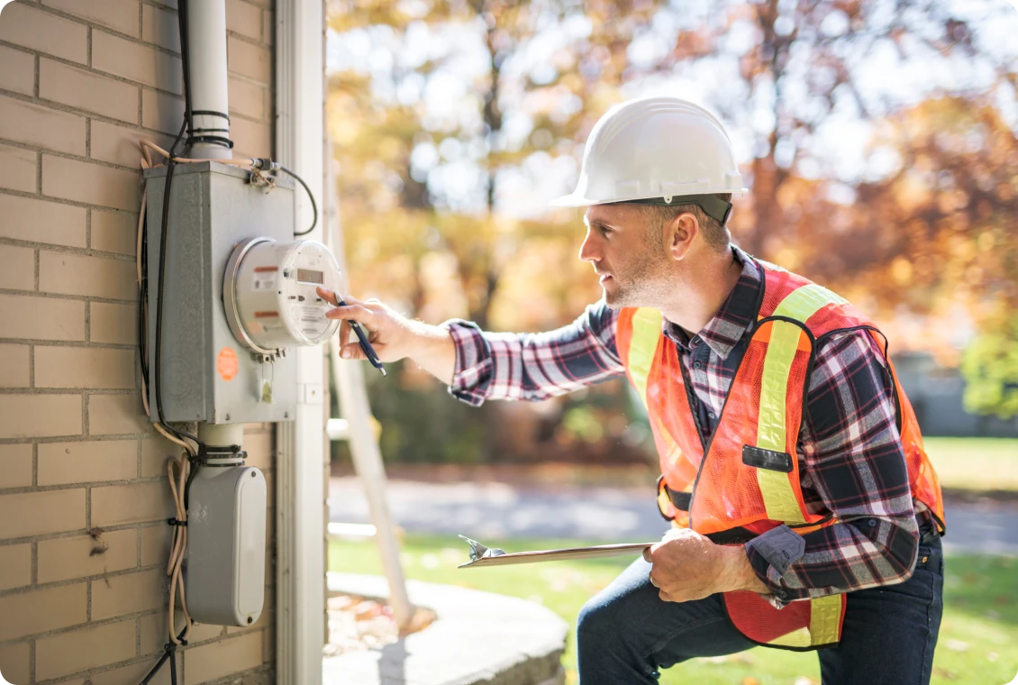 Worker inspecting outdoor electrical meter on building.
